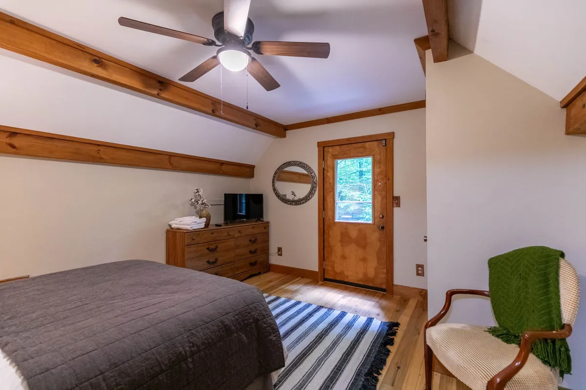 This image showcases a cozy corner featuring rustic wooden beams, a mirror reflecting natural light, a striped rug, a door that hints at access to the outdoors, a chest of drawers, and a television. The scene has a relaxed, inviting atmosphere, suggesting a place to unwind after a mountain adventure, with subtle connections to the outdoor environment through its materials and light.