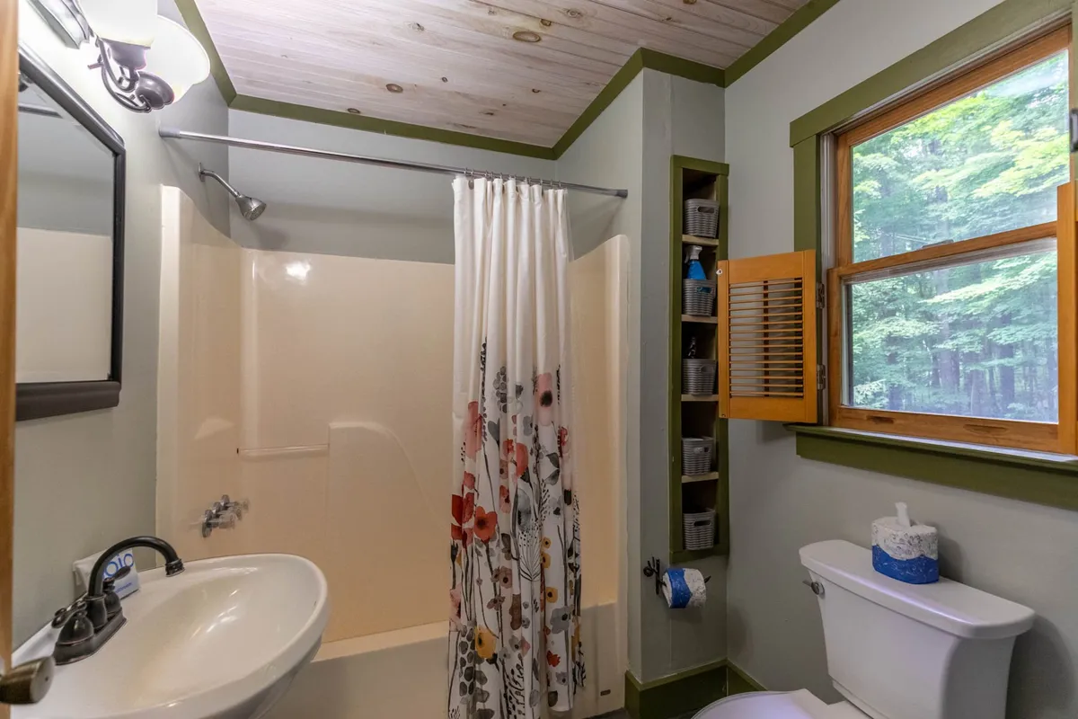 A bright bathroom with a flower-patterned shower curtain, a window overlooking greenery, and a sink with a large mirror. The space is fresh, rejuvenating, and filled with natural light, offering a spa-like atmosphere for guests to refresh.