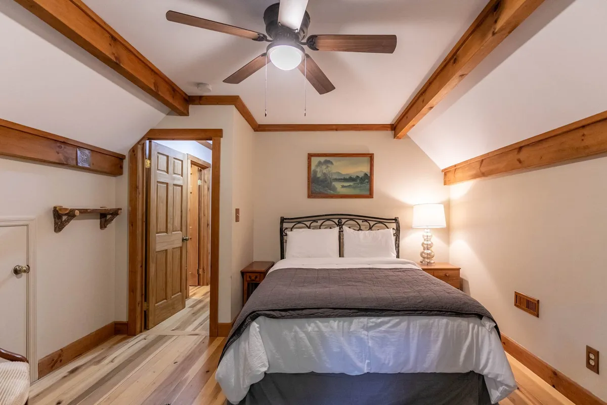 A cozy King bedroom with a large bed, nightstand, ceiling fan, and subtle wall art. Soft morning light filters in, emphasizing the serene mood and inviting guests to unwind.