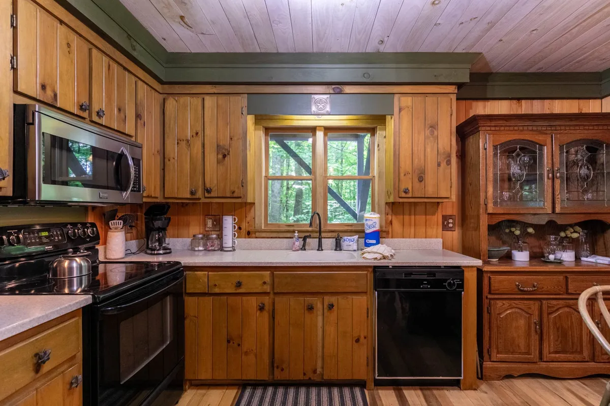 A cozy kitchen featuring warm wooden cabinets, a kitchen island, stainless steel appliances, and a window framing lush greenery. The setting is inviting, with everything arranged for easy meal preparation and family gatherings.