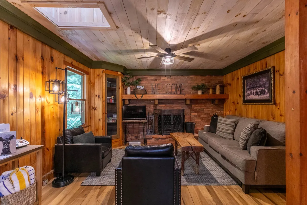 A warm and inviting living area featuring soft lighting, a welcoming fireplace, comfortable sofa, wooden walls, and tasteful light fixtures. The 'WELCOME' sign and overall ambiance evoke a sense of hospitality and belonging, inviting guests to relax and connect.