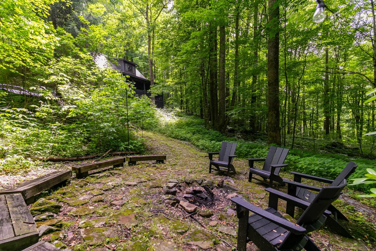 An inviting outdoor fire pit area surrounded by wooden seating and lush greenery. The fire pit provides a focal point for gatherings, storytelling, and stargazing, set in a relaxed, natural environment.