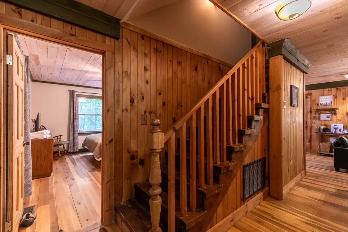 This image presents a cozy living area with prominent wooden staircase, wall paneling, and a doorway leading to a bedroom. The space is warm and inviting, perfect for gathering after a day outdoors, and the wood finishes echo the surrounding forest environment.